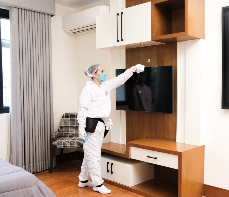 VIDERR technician in a white uniform detail-cleaning a wall-mounted TV and cabinetry